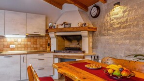 A kitchen with a stone wall, wooden ceiling beams, and a rustic wooden table with fruit. - Cozy apartment in Medulin with WiFi (Medulin)