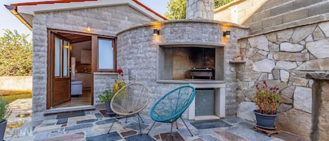 Un edificio de piedra con chimenea, dos sillones y una planta en maceta.