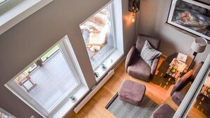 Et værelse med udsigt til en have, en stol, et bord med en lampe og et billede i ramme på væggen.