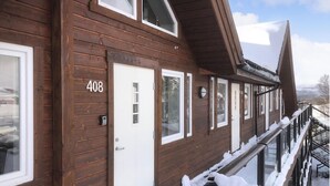 En træbygning med nummer '408' på døren, flere vinduer og en balkon med sne.