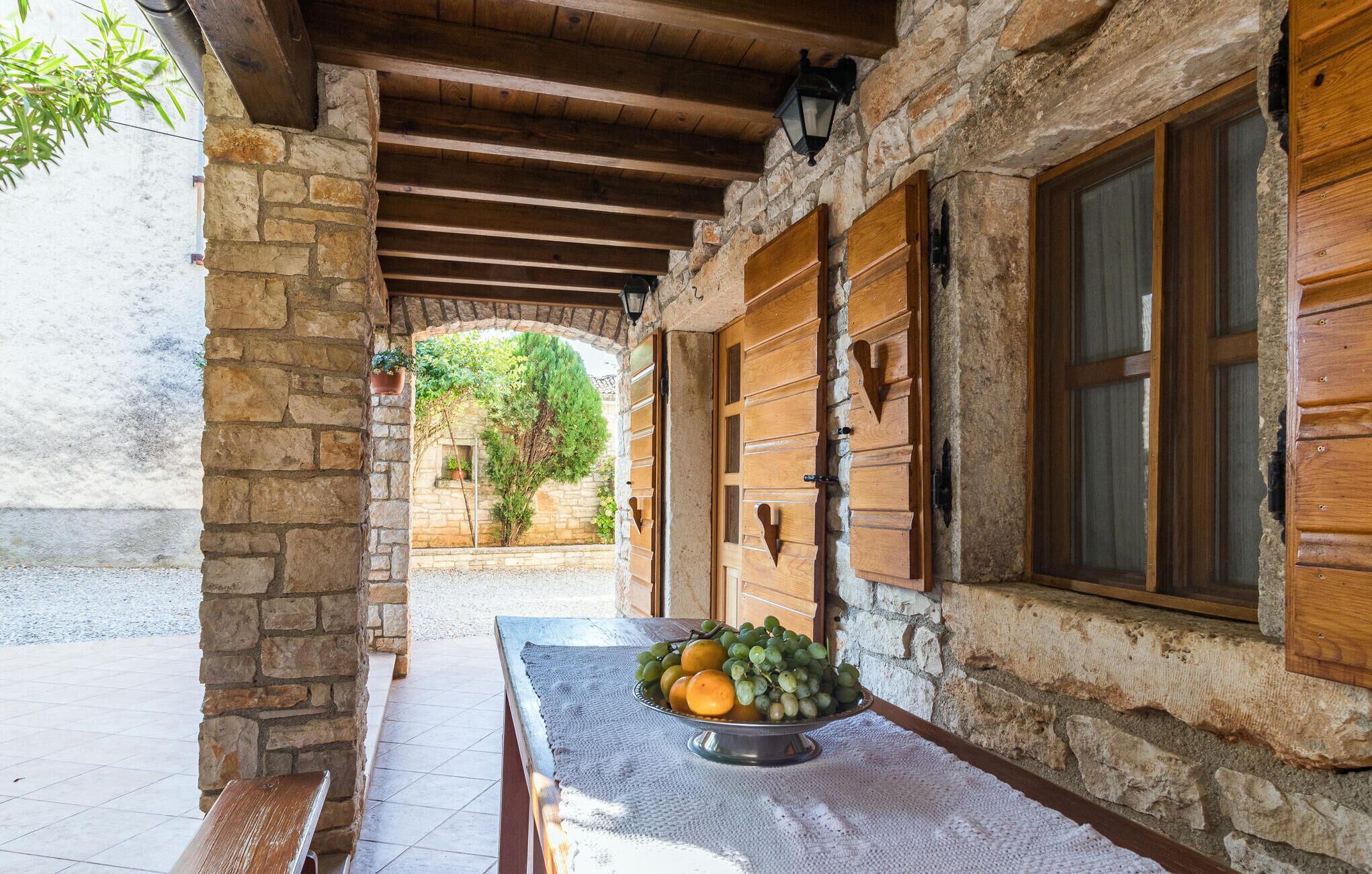 Un edificio de piedra con contraventanas de madera y un cuenco de metal con fruta sobre una mesa.