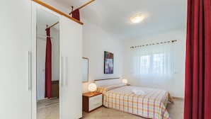 Une chambre à coucher avec un lit, une table de chevet, un miroir et une fenêtre avec des rideaux.