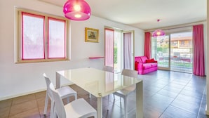 Una sala de estar moderna con una mesa blanca, dos sillas blancas, un sofá rosa y un ventanal con cortinas rosas.