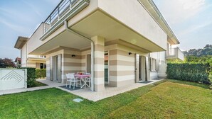 Una casa moderna de dos pisos con un porche cubierto, un pequeño jardín y una mesa de comedor para cuatro.