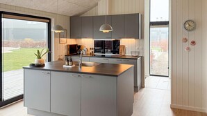 Una cocina moderna con armarios grises, una isla central, luces colgantes y vistas al exterior.
