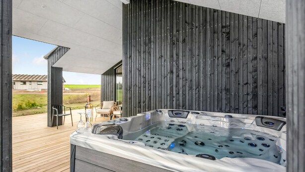 Un moderno jacuzzi al aire libre con una terraza de madera y vista a un paisaje rural.