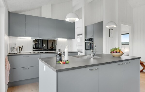 Enjoy cooking in this well-equipped kitchen with a central island, coffee maker, kettle, and wine bottle, offering a view of the outdoors.