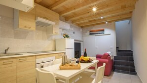A modern kitchen with wooden cabinets, a white countertop, and a dining area with a table and chairs. - 2 bedroom gorgeous apartment in Monte Isola (Monte Isola)