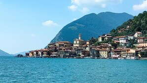 A coastal town with buildings along the waterfront, a prominent mountain in the background, and calm blue waters. - 2 bedroom gorgeous apartment in Monte Isola (Monte Isola)