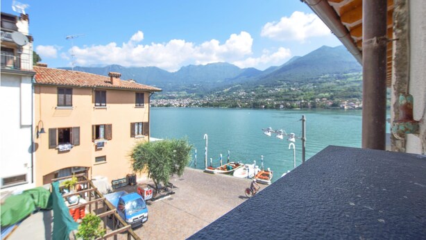 A view of a lake with boats, a building with a tiled roof, and mountains in the background. - 2 bedroom gorgeous apartment in Monte Isola (Monte Isola)