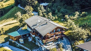 Un grand chalet en bois doté de nombreux balcons et d’un vaste patio entouré d’une végétation luxuriante.