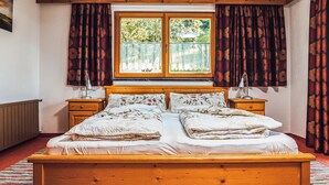 Un lit double avec une literie à motifs floraux, une tête de lit en bois, deux tables de chevet avec des lampes et une fenêtre avec des rideaux.