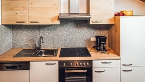 Une cuisine compacte dotée de meubles en bois, d’un évier en acier inoxydable, d’une machine à café et d’un four encastré.