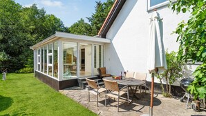 Ein modernes Haus mit Wintergarten, Sitzgelegenheiten im Freien und einem Garten.