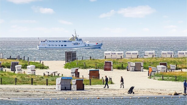 A beach with a ferry, portable toilets, and a person walking. - Stunning home in Büsum with sauna (Büsum)
