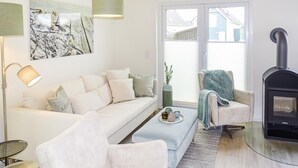 A modern living room with a sofa, armchairs, a coffee table, a fireplace, and a large window with blinds. - Stunning home in Büsum with sauna (Büsum)