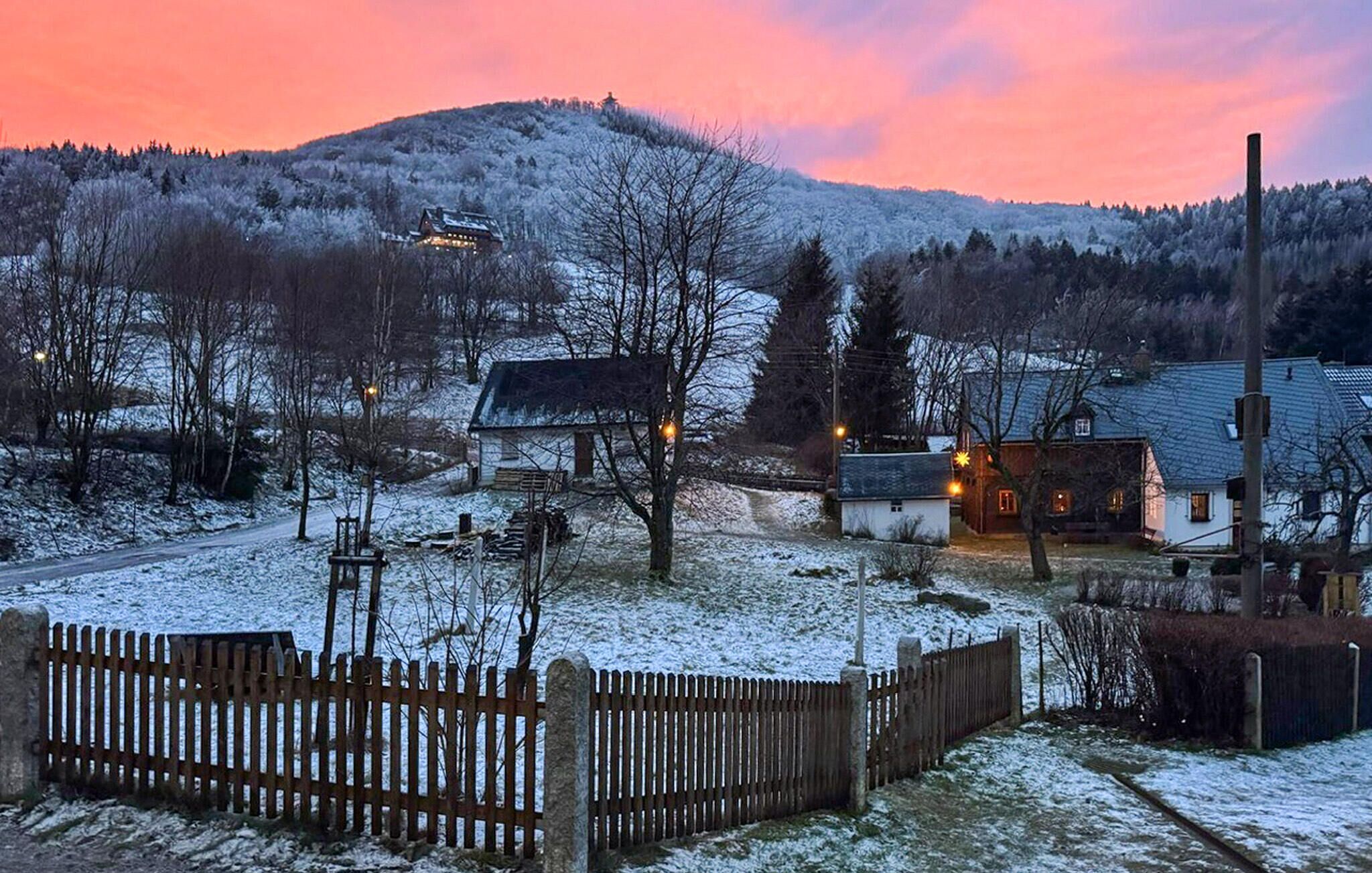 Ein verschneites Dorf mit Holzzäunen und Häusern mit erleuchteten Fenstern.