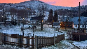 A rural village with snow-covered ground, wooden fences, and houses with lit windows. - Ferienhaus Lausche Haeusl (Waltersdorf)