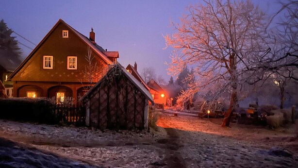 A rustic house with a stone exterior and a wooden roof, surrounded by a snowy landscape at dusk. - Ferienhaus Lausche Haeusl (Waltersdorf)