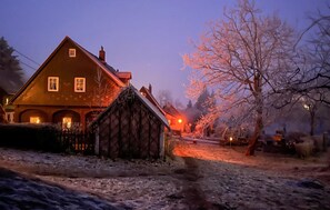 Una casa rústica amb façana de pedra i teulat de fusta, envoltada d'un paisatge nevós a l'hora del vespre.