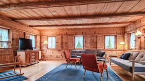 A cozy log cabin interior with a wooden ceiling, a TV, a sofa, a dining table with chairs, and a blue rug. - Ferienhaus Lausche Haeusl (Waltersdorf)