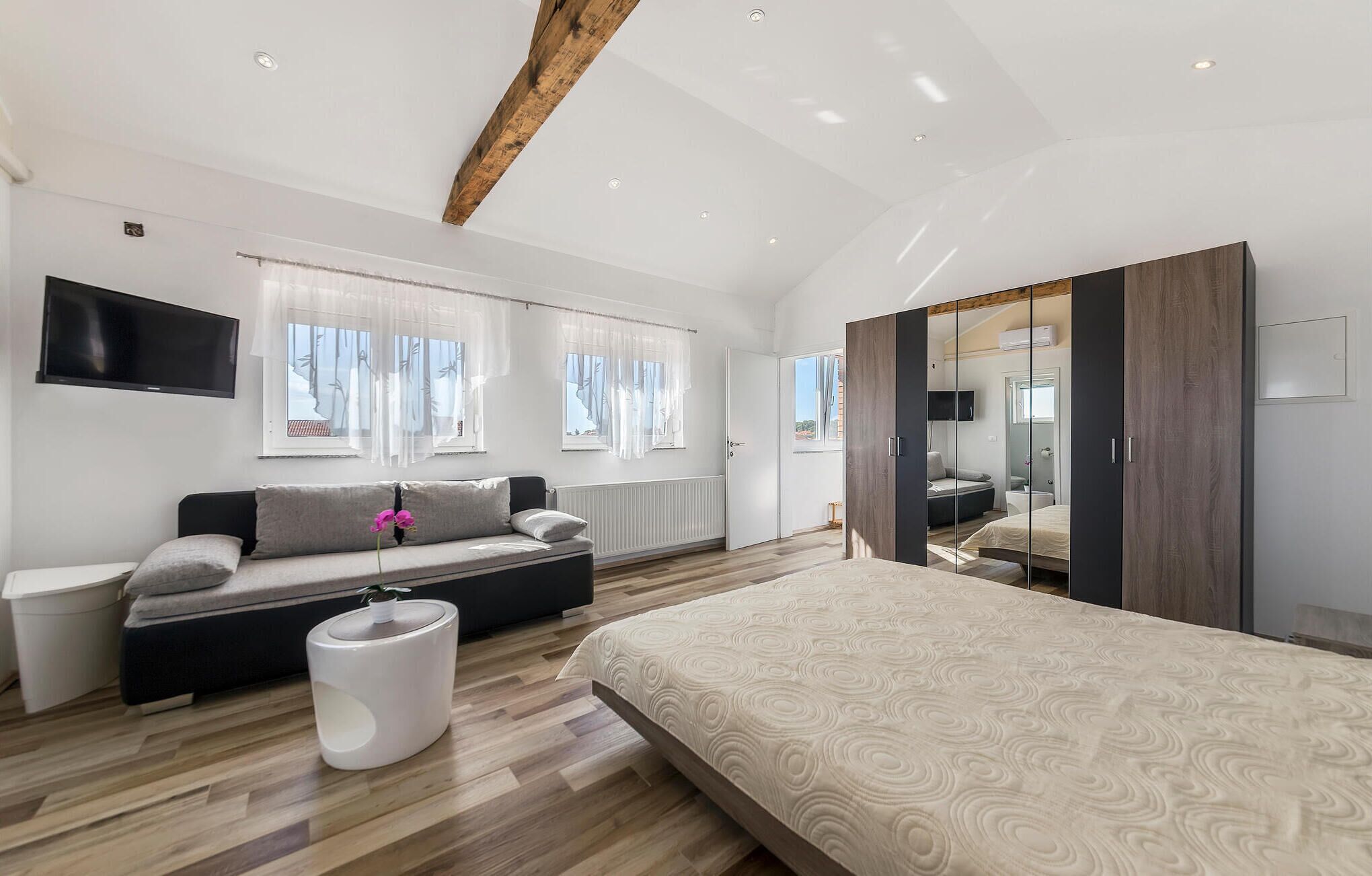 A modern bedroom with a large bed, a sofa, a TV, and a mirror.