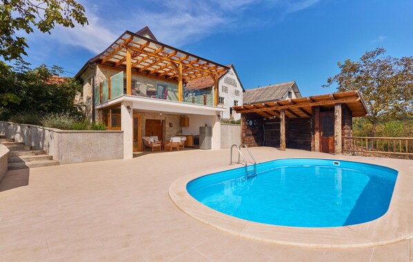 Une maison à deux étages avec une piscine, une pergola en bois et des murs en pierre.