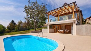 Ein modernes Haus mit Wintergarten, Schwimmbad und einer Terrasse mit Gartenmöbeln.