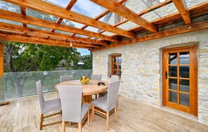 Une terrasse dallée de pierres, avec une table et des chaises en bois, un panier de fruits et une porte en bois.