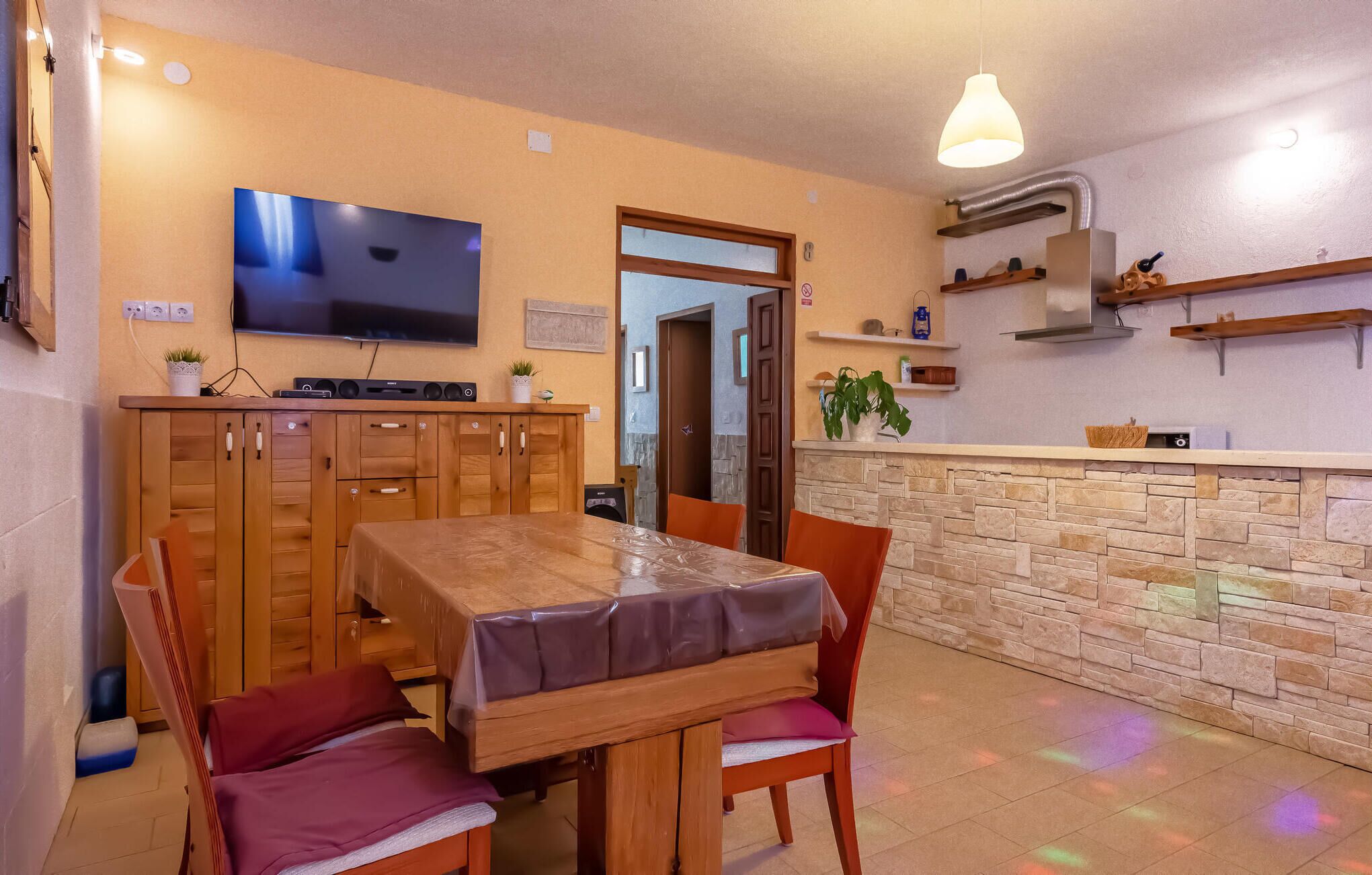 Un comedor con una mesa de madera, sillas y un televisor montado en la pared.