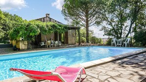 A swimming pool with a stone border, a red lounge chair, and a small building with a tiled roof. - Beautiful home in Caux (Caux)