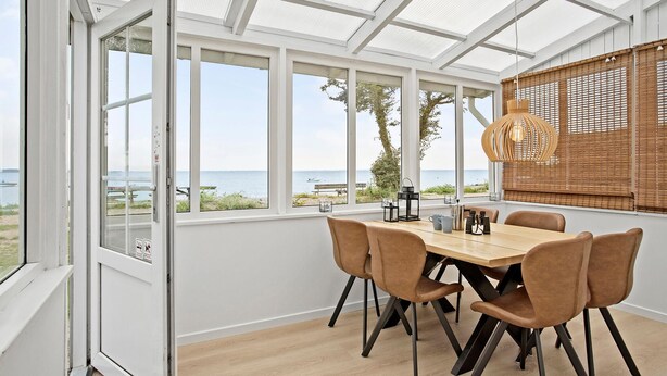 A dining area with a table and chairs, large windows, and a view of the sea. - Beach front home in Sjølund (Sjølund)