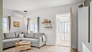 A modern living room with a grey sectional sofa, a round wooden coffee table, and a white wardrobe. - Beach front home in Sjølund (Sjølund)