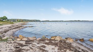 A beach with a rocky shoreline, calm water, and a distant view of houses and hills. - Beach front home in Sjølund (Sjølund)