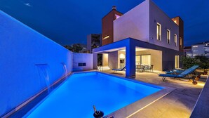 Ett modernt hus med en swimmingpool, utomhusmöbler och en väl upplyst uteplats.