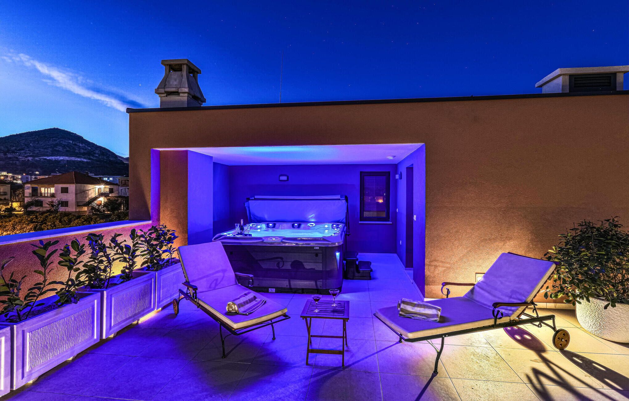 A rooftop terrace with a hot tub, lounge chairs, and potted plants.