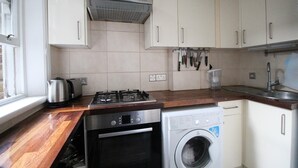 Una cocina con armarios blancos, estufa a gas, lavadora y una ventana.