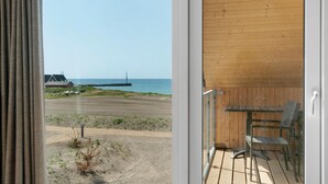Un balcón con vista a una playa, una estructura de madera y un faro distante.