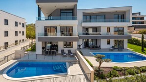A modern multi-story residential building with a rooftop terrace, two swimming pools, and outdoor seating areas.