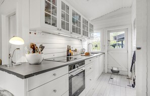 Una cocina con armarios blancos, horno empotrado y ventana con vistas a una casa.