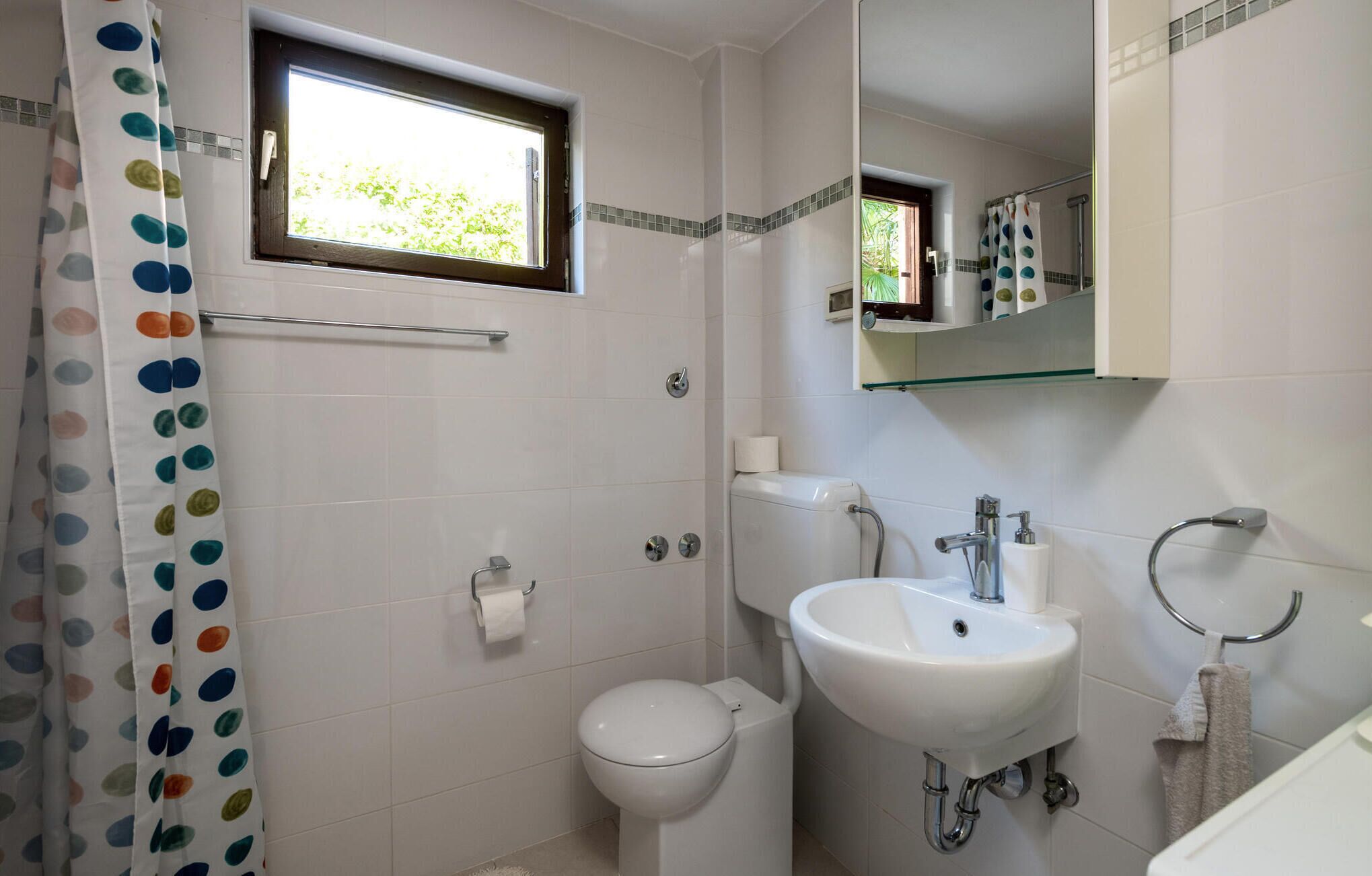 Une salle de bain avec des toilettes, un lavabo et une fenêtre située au-dessus des toilettes.