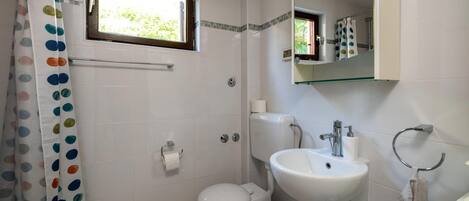 Une salle de bain avec des toilettes, un lavabo et une fenêtre située au-dessus des toilettes.