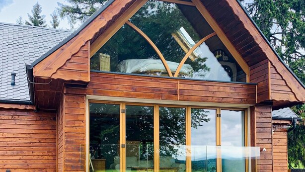 Eine Holzhütte mit einer großen Glasschiebetür, einem Satteldach und einem sichtbaren Innenraum mit einem Bett und einem Fenster.