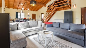 Amplia sala de estar con techo alto, una escalera de madera y un rincón acogedor con dos sofás y una mesita de centro.
