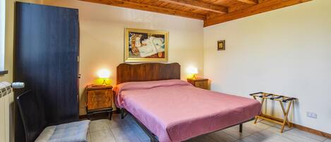 A bedroom with a bed, two bedside tables, a chair, a wooden bench, a painting on the wall, and a skylight.