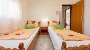 Habitación doble con dos camas individuales, un armario de madera, una mesita de noche pequeña y una puerta que da a otra habitación.