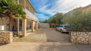 Una propiedad residencial con un espacio exterior techado, un coche estacionado en la entrada y un muro de piedra.
