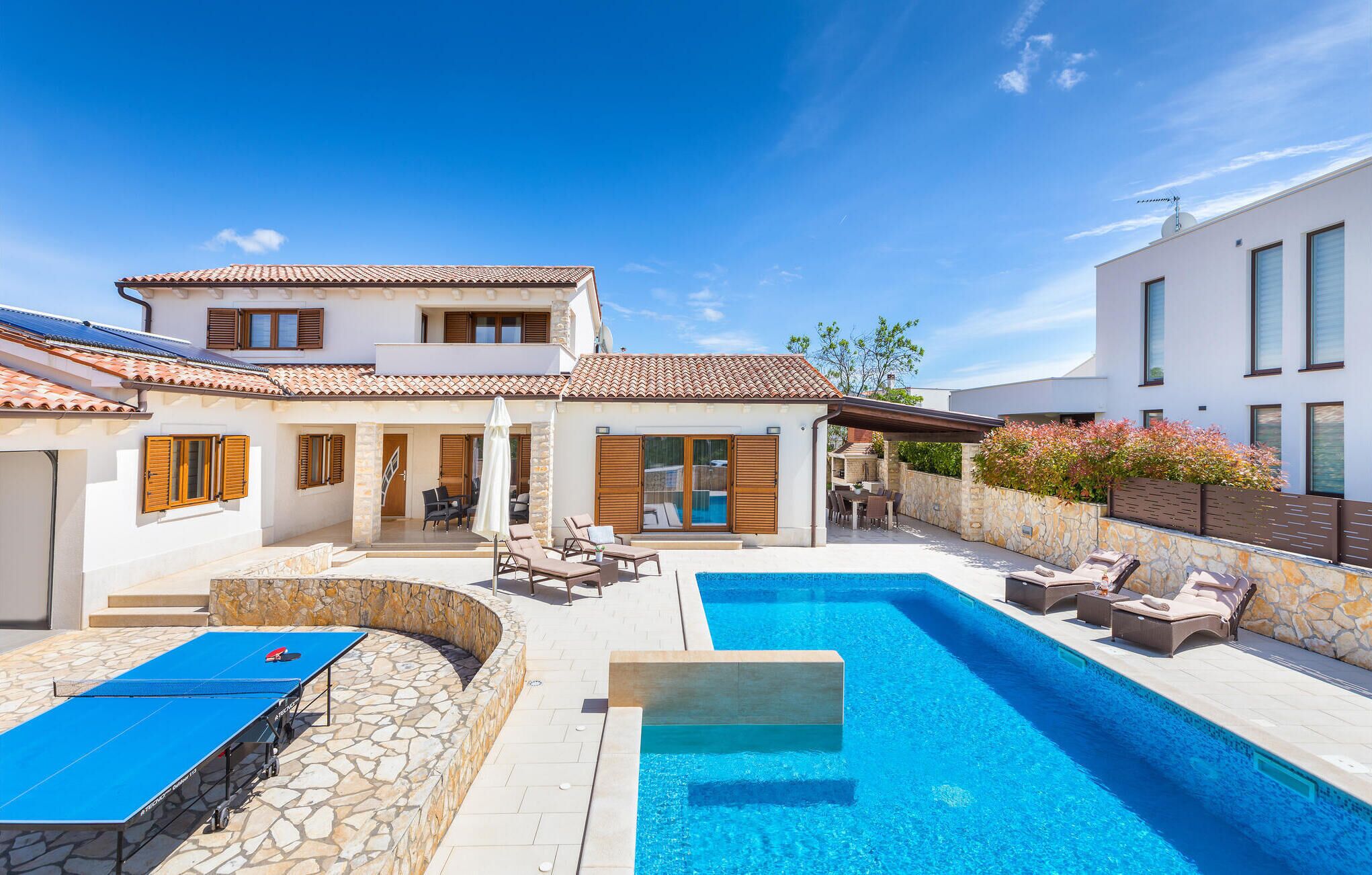 A modern house with a swimming pool, outdoor seating, and a ping pong table.