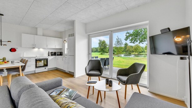 A modern kitchen with white cabinets, a dining area with a table and chairs, a sofa, and a TV on the wall.