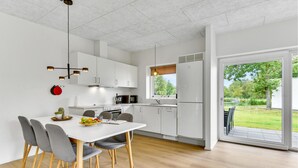A modern kitchen with white cabinets, a dining table with chairs, and a view of a garden through a sliding glass door.